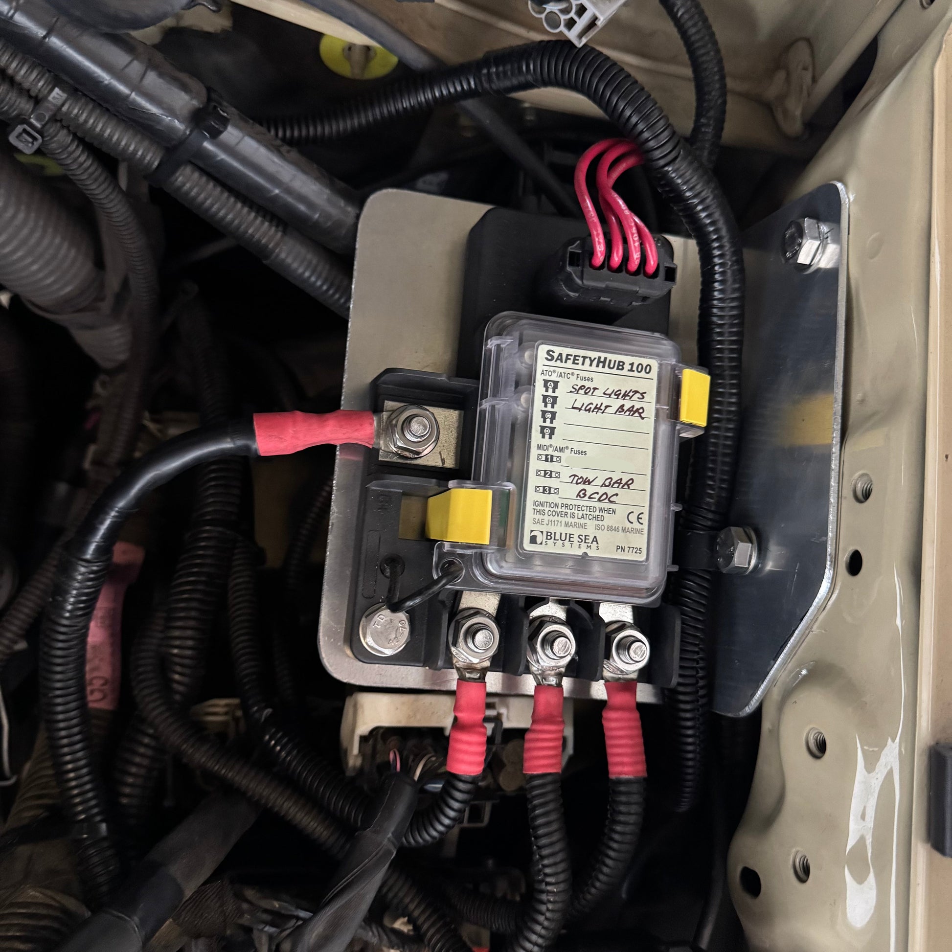 Car battery safety hub with wires and connectors in a vehicle's engine compartment.
